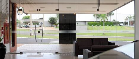 A hotel lobby with a reception desk, a seating area, and a view of the street outside.