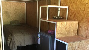 Ein kleines Zimmer mit einem Etagenbett, einem kleinen Kühlschrank und einer Holzregaleinrichtung.
