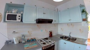 A compact kitchen with light blue cabinets, a microwave, a stove, and a sink. - Blue House Beach Apartment - Sleeps 4 & Balcony (Rhodes)