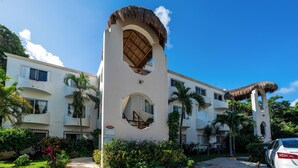 A hotel with a central tower featuring a thatched roof, surrounded by lush greenery and palm trees. - Sueño - Playacar 2 Rosa Blanca - 2 BR (Playa del Carmen)