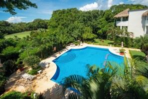 A pool surrounded by lush greenery and a white building with a thatched roof.
