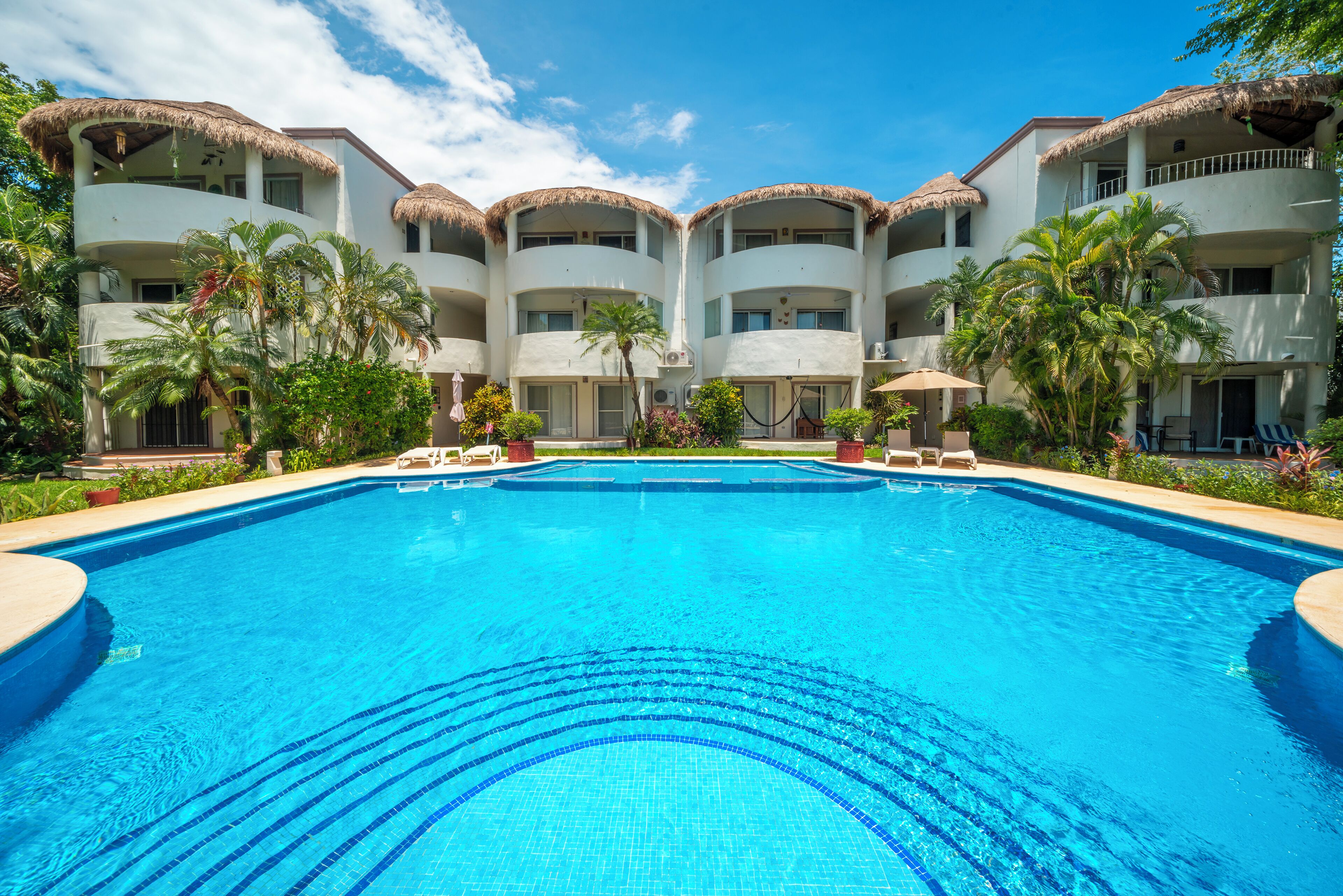 A hotel with a central swimming pool, multiple balconies, and tropical landscaping.
