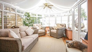 A sunroom with wicker furniture, large windows, and a ceiling fan.