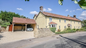 A two-story house with a red-tiled roof, a covered carport, and a stone wall.