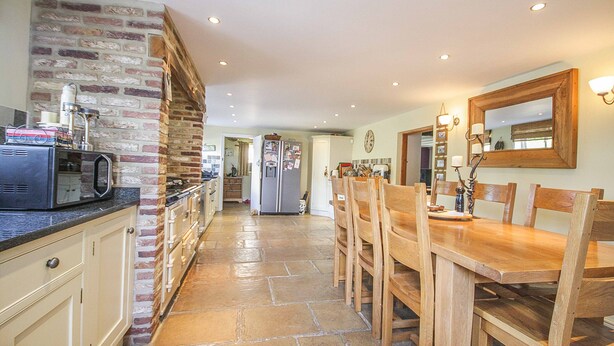 A kitchen with a brick wall, a wooden dining table, and a refrigerator.