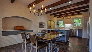A kitchen with a brick fireplace, wooden beams, and a dining area with leather chairs.
