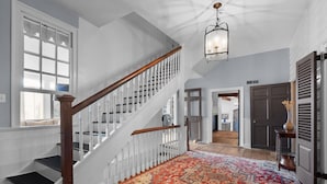 A staircase with white railings and a wooden handrail, leading to a landing with a patterned rug.