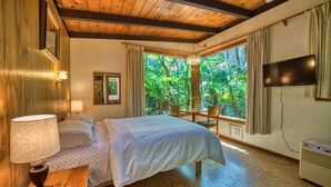 Un dormitorio con cama, mesita de noche, lámpara, televisor y ventana con cortinas.