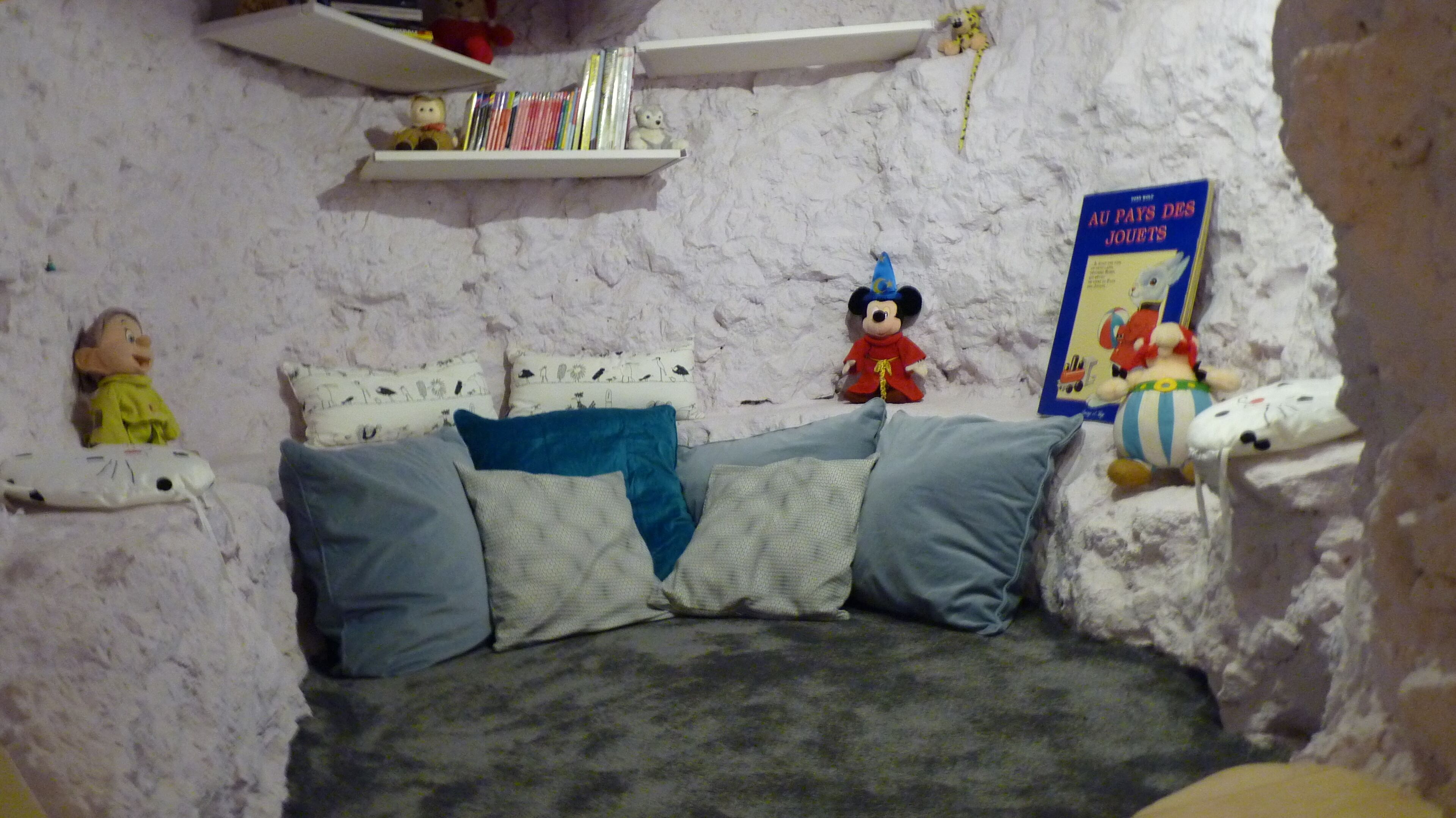 A cozy room with a bed, pillows, and shelves with books and stuffed toys.