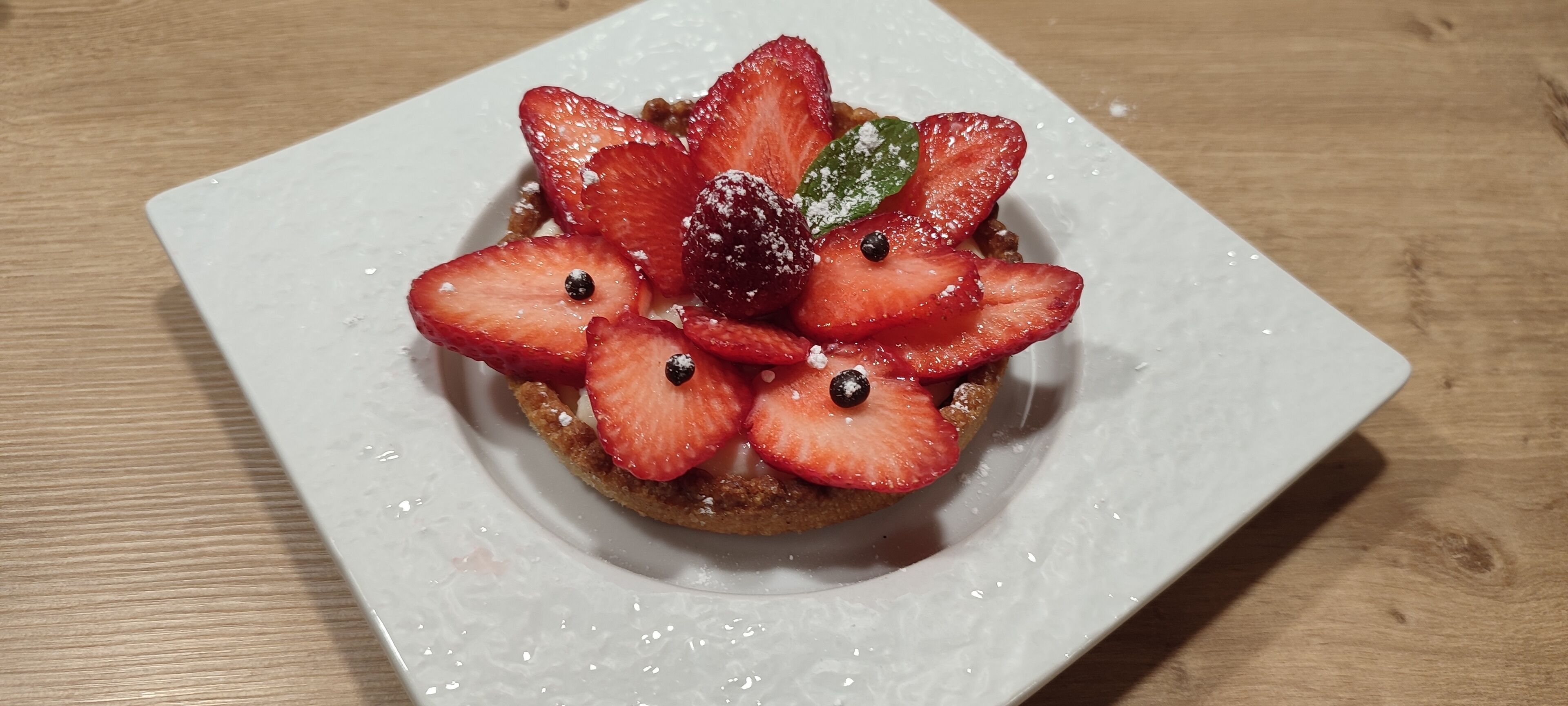 Een vierkant bord met een dessert, afgetopt met aardbeien en een bessenfruit.