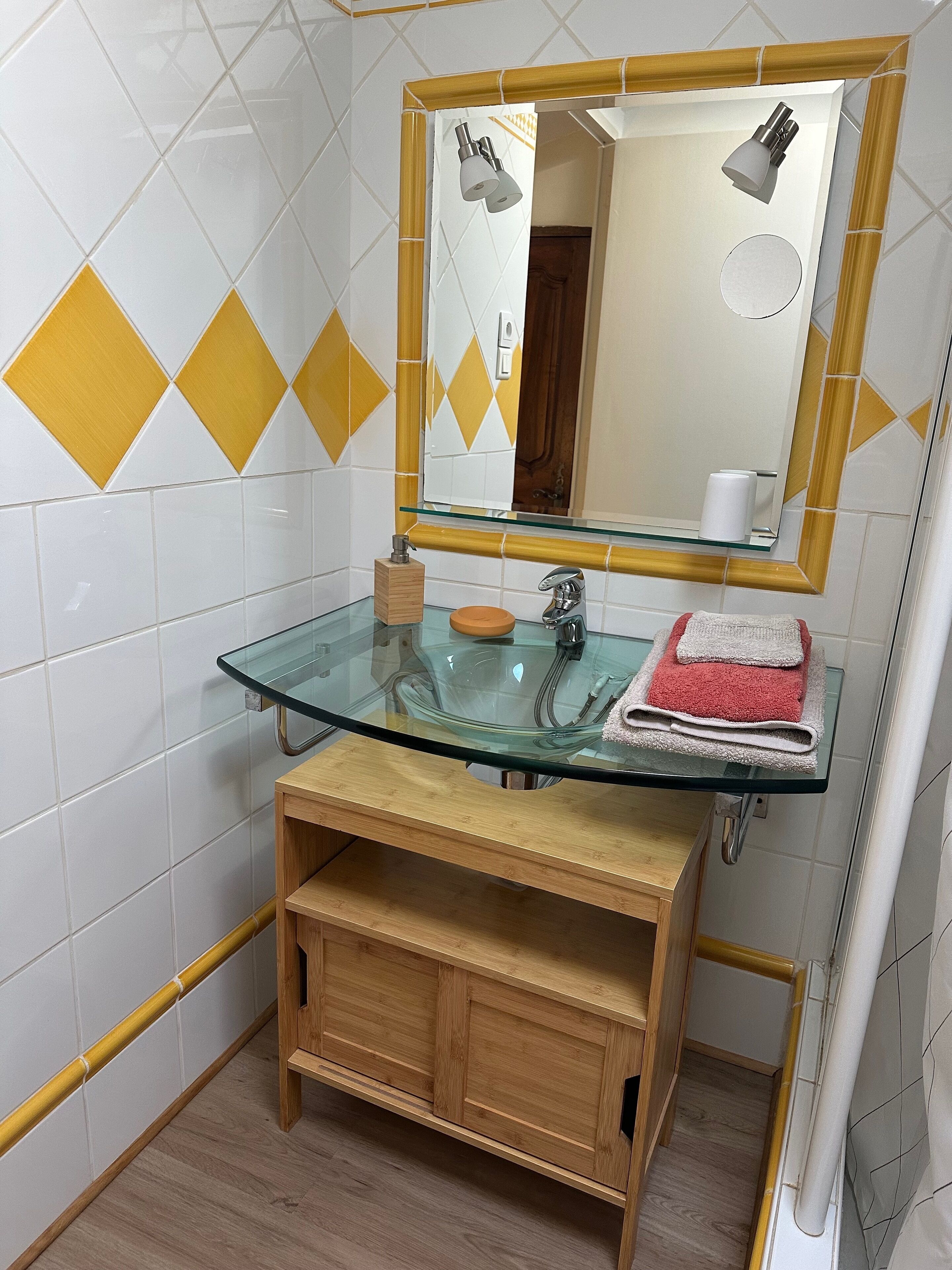 A bathroom with a glass sink, wooden vanity, and a mirror with a light fixture.