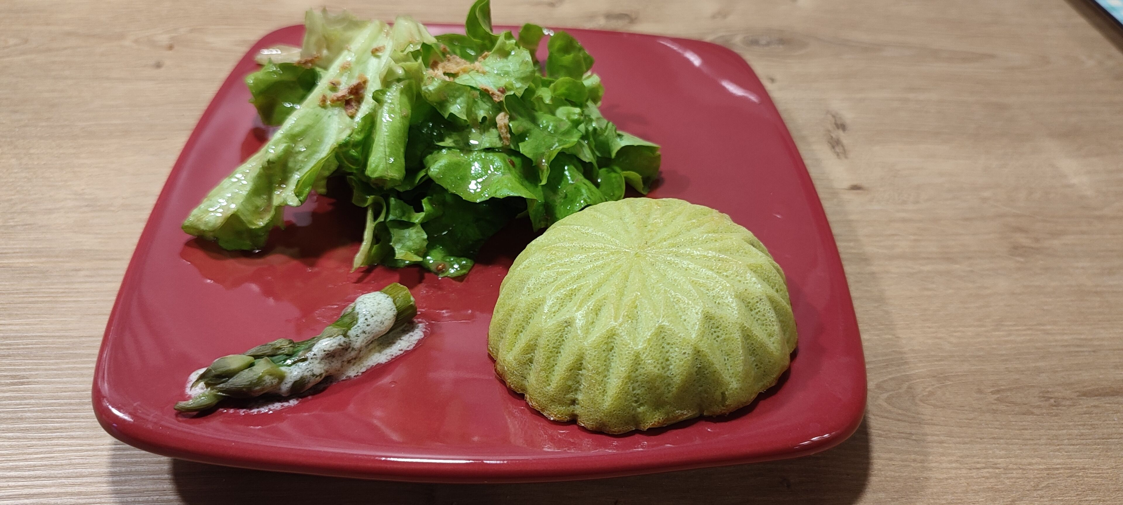 Un plato rojo con un vegetal verde, posiblemente espárragos, y un elemento verde y redondo, probablemente una verdura o fruta.