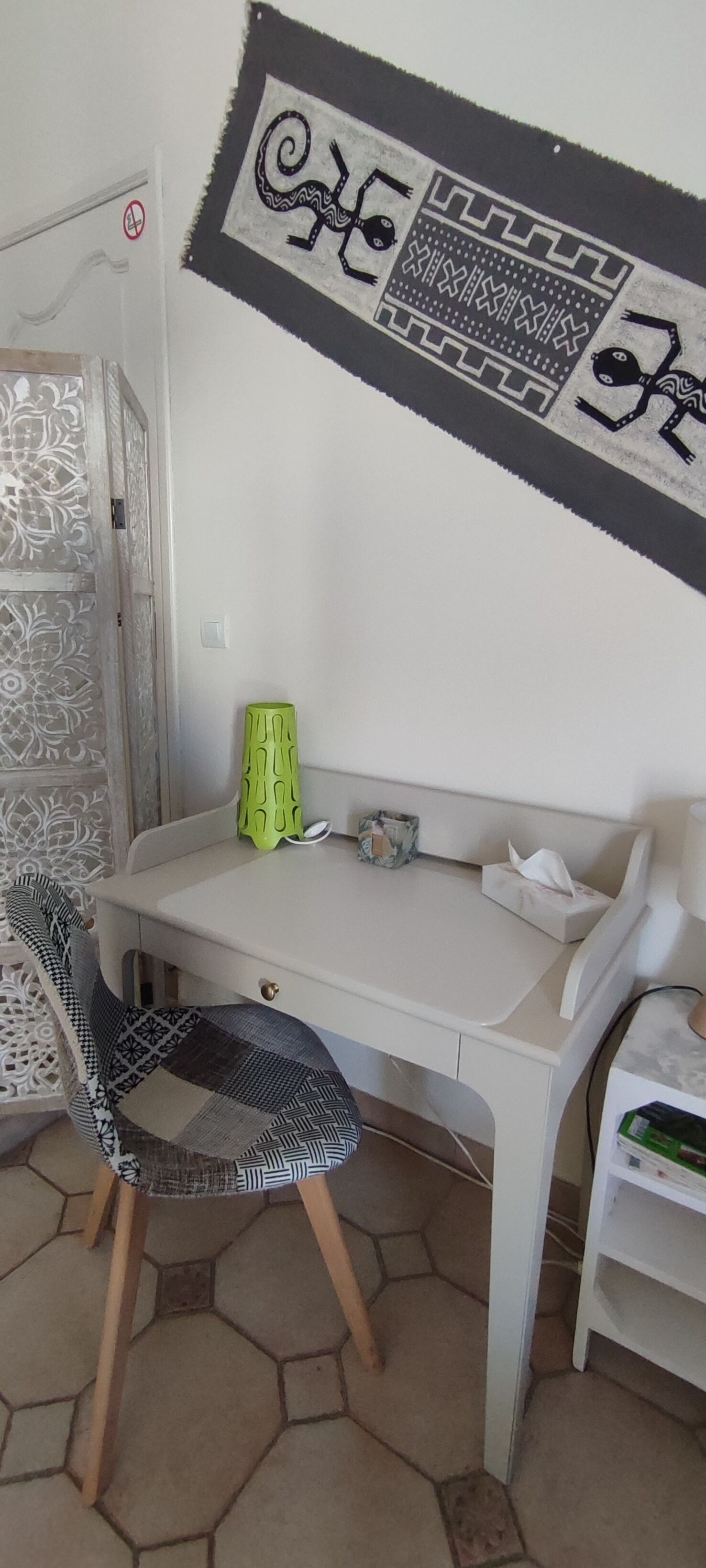 Une petite pièce avec une table blanche, une chaise à motifs et un élément décoratif mural.