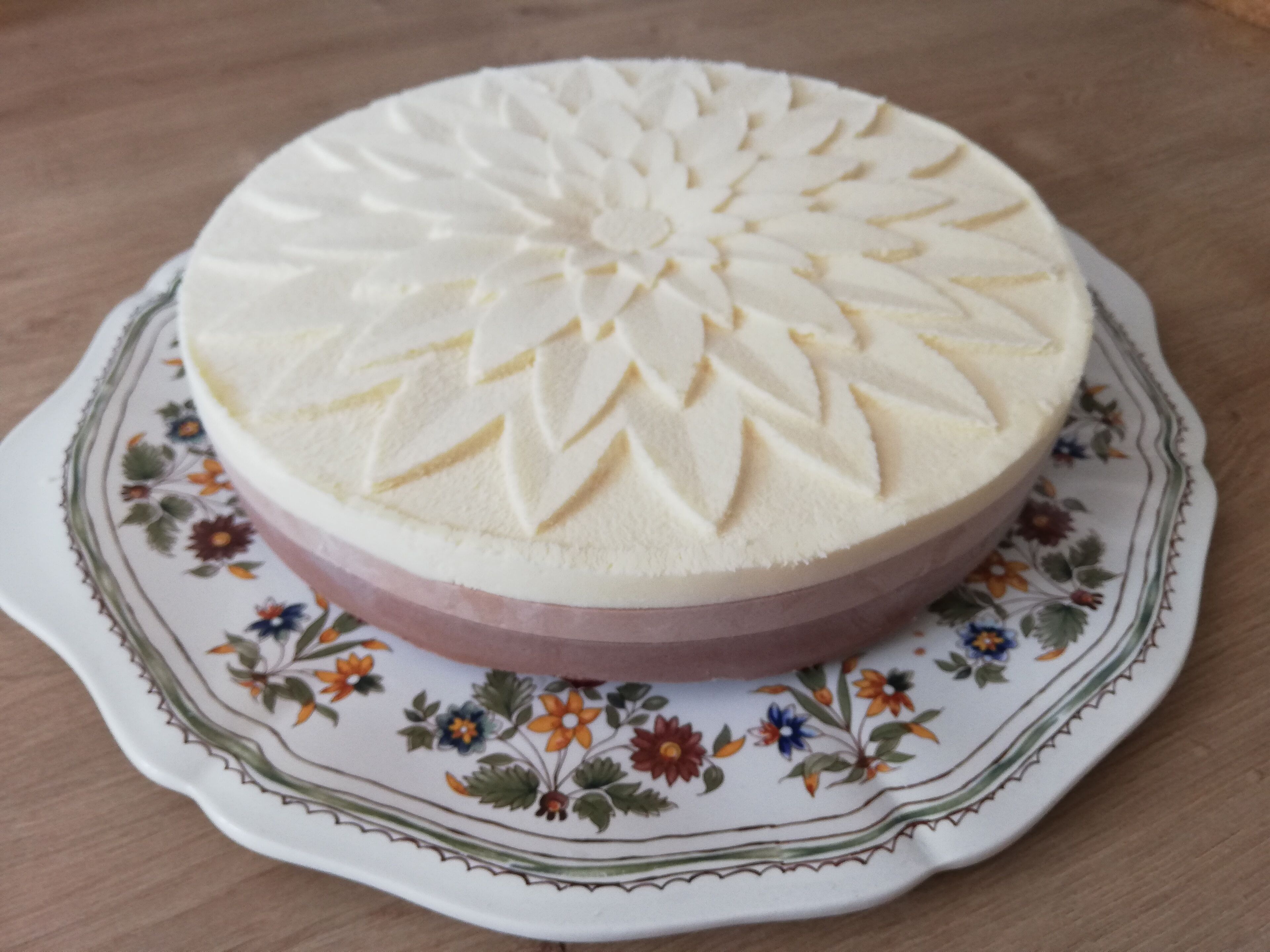 Un pastel redondo con un diseño detallado en la parte superior, sobre un plato con estampado floral.