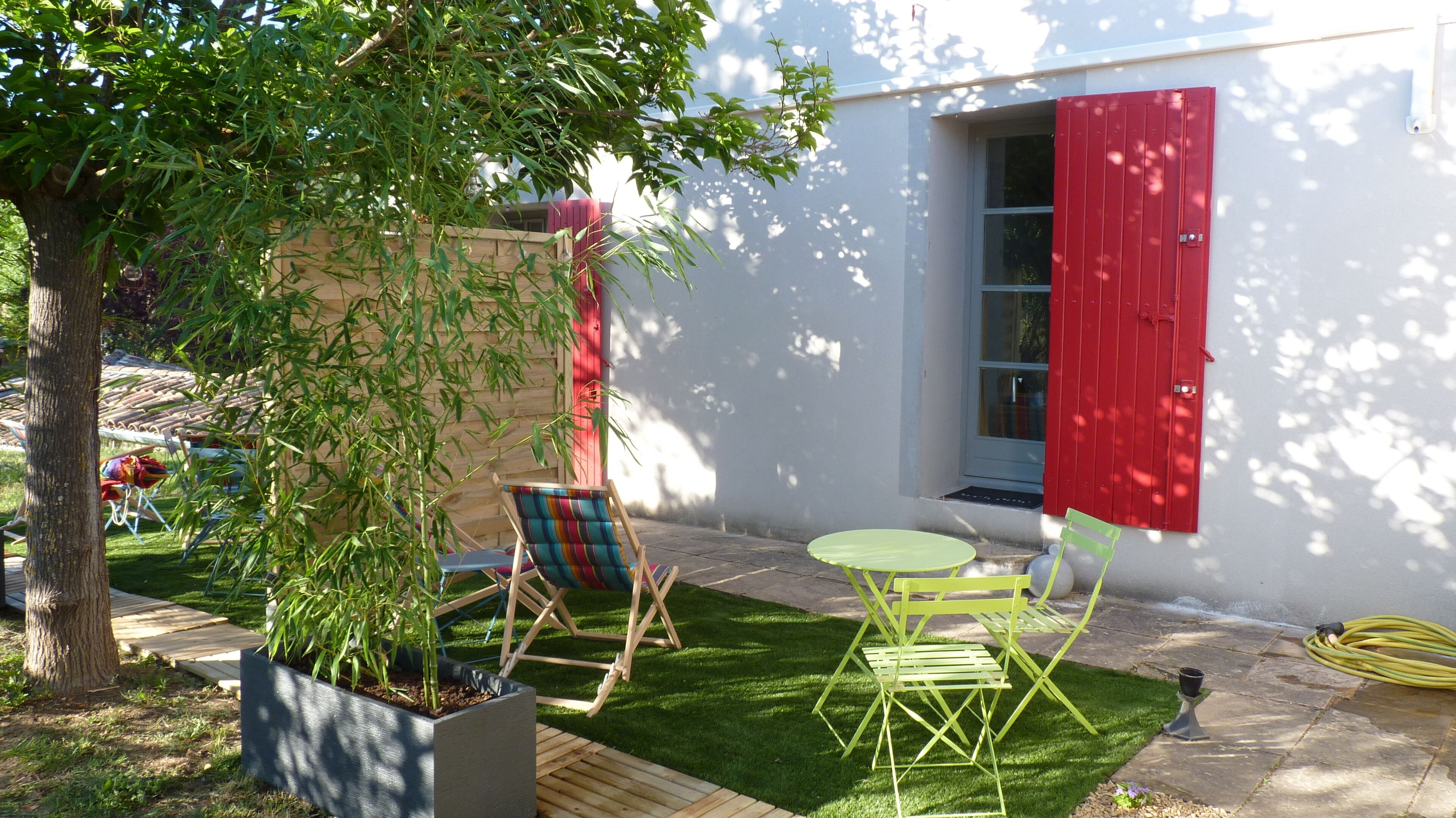 A small patio with a table and chairs, a potted plant, and a red door.