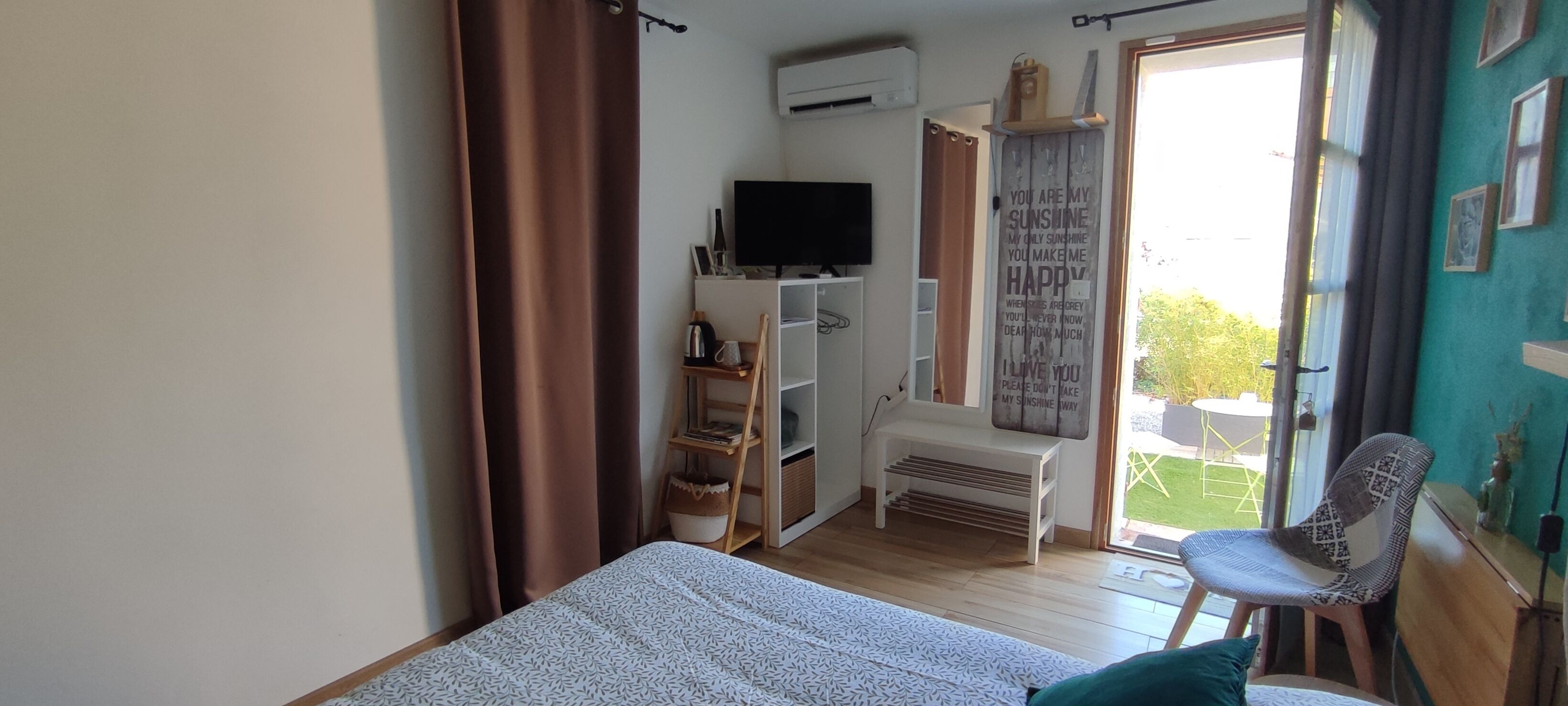 A bedroom with a bed, a TV, a shelf with books, and a balcony with a chair.