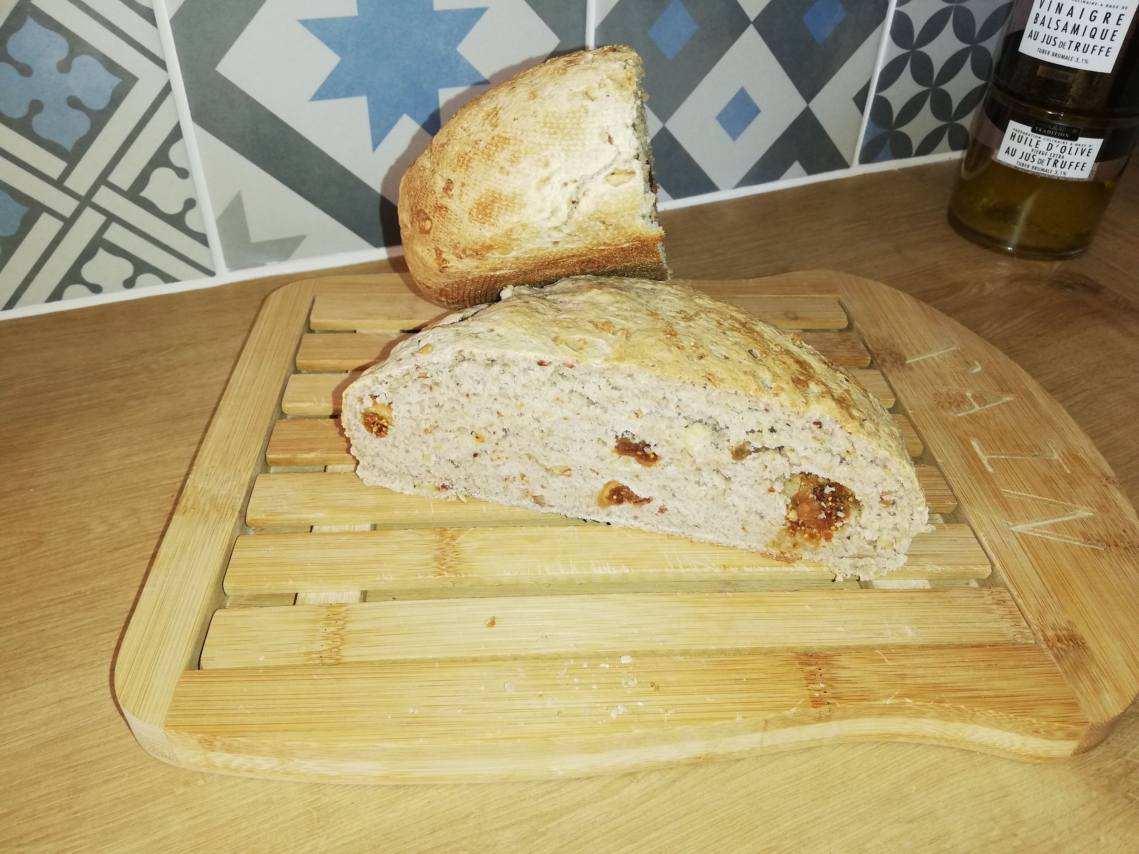 A loaf of bread on a wooden cutting board with a patterned tile backsplash in the background.