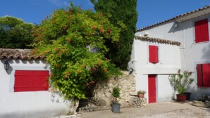 Un bâtiment traditionnel, de couleur blanche, avec des volets rouges et un mur en pierre.