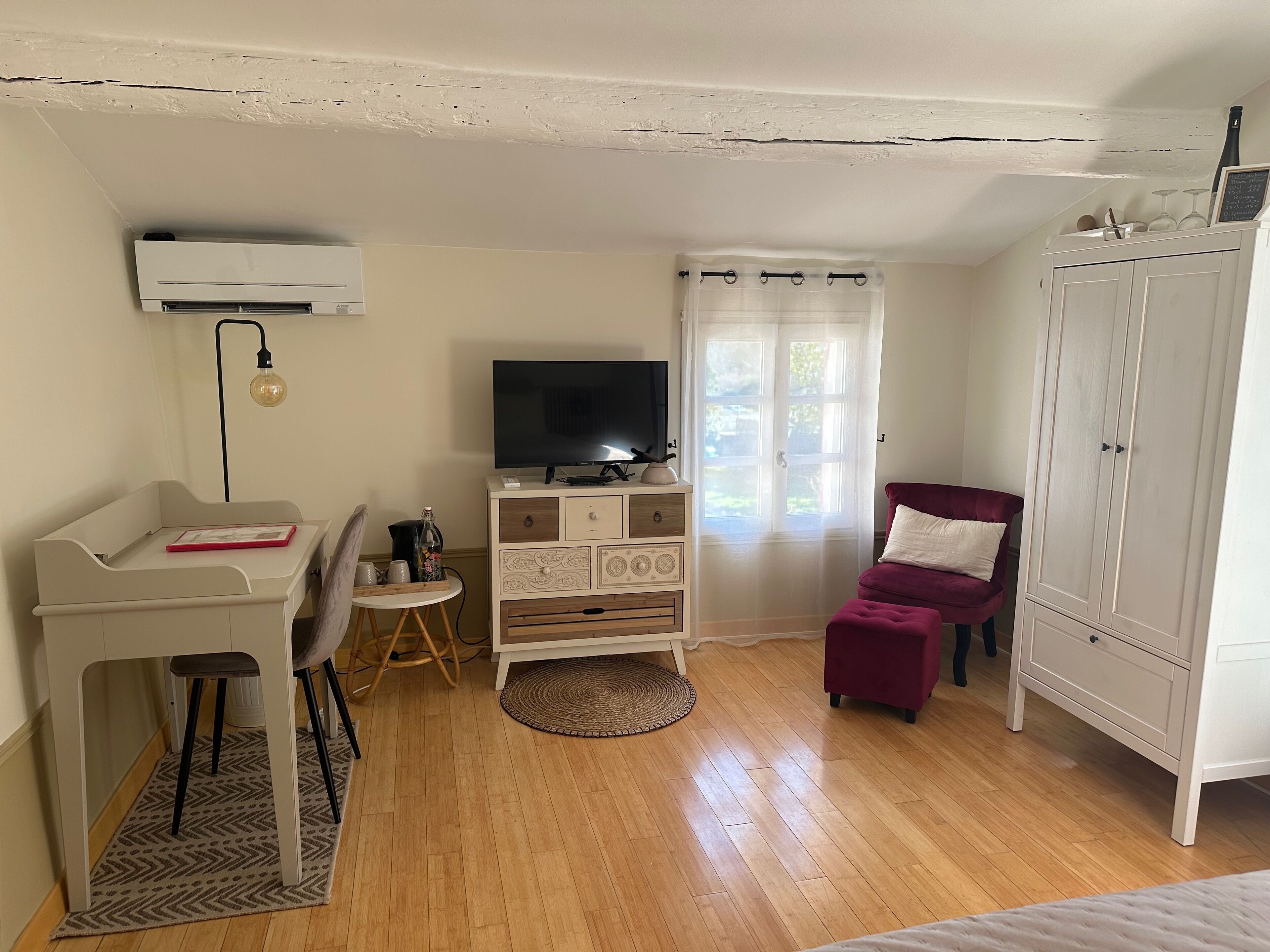 A room with a desk, chair, television, wardrobe, and a window with curtains.