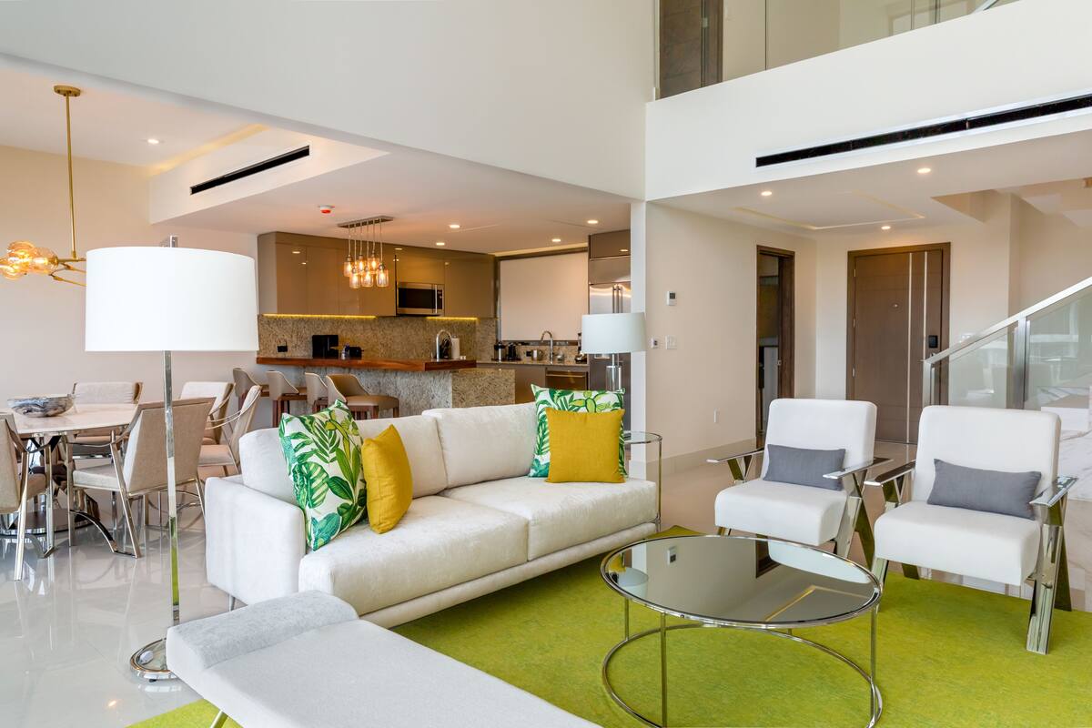 A modern living room with a sofa, chairs, a glass coffee table, and a dining area with chairs and a table.