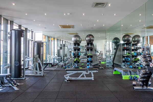 A modern gym with various exercise equipment, large mirrors, and ample natural light.