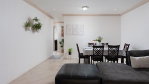 A modern living room with a black leather sofa, a dining table with chairs, and a small side table with a plant. -  A charming blend of comfort and sophistication in this near-the-beach townhouse (Holetown)