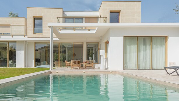 Ett modernt hus med en swimmingpool, stora fönster och ett platt tak.
