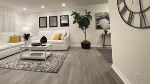 Ein modernes Wohnzimmer mit einem weißen Sofa, einem Couchtisch, einer großen Topfpflanze und einer Wanduhr.