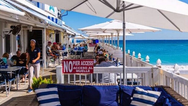 Ein Außenbereich mit Sonnenschirmen, ein Schild, das keinen Zugang zum Steg erlaubt, und der Blick auf das Meer.