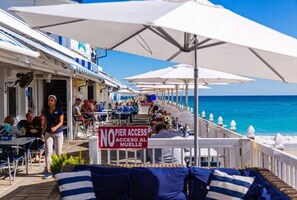 Een terras met parasols, een bordje dat toegang tot de pier verbiedt, en uitzicht op de oceaan.