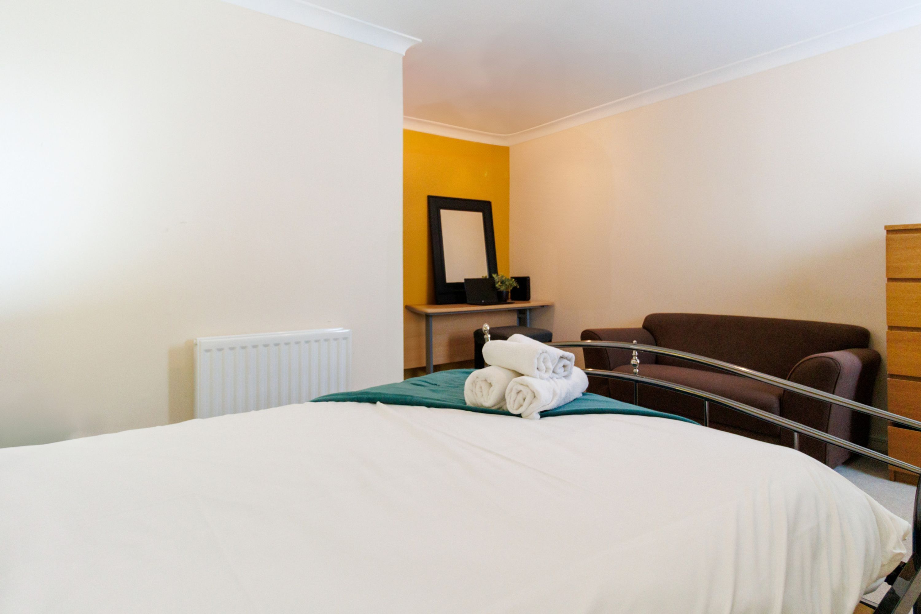 A hotel room with a bed, a chair, a dresser, and a mirror on the wall.