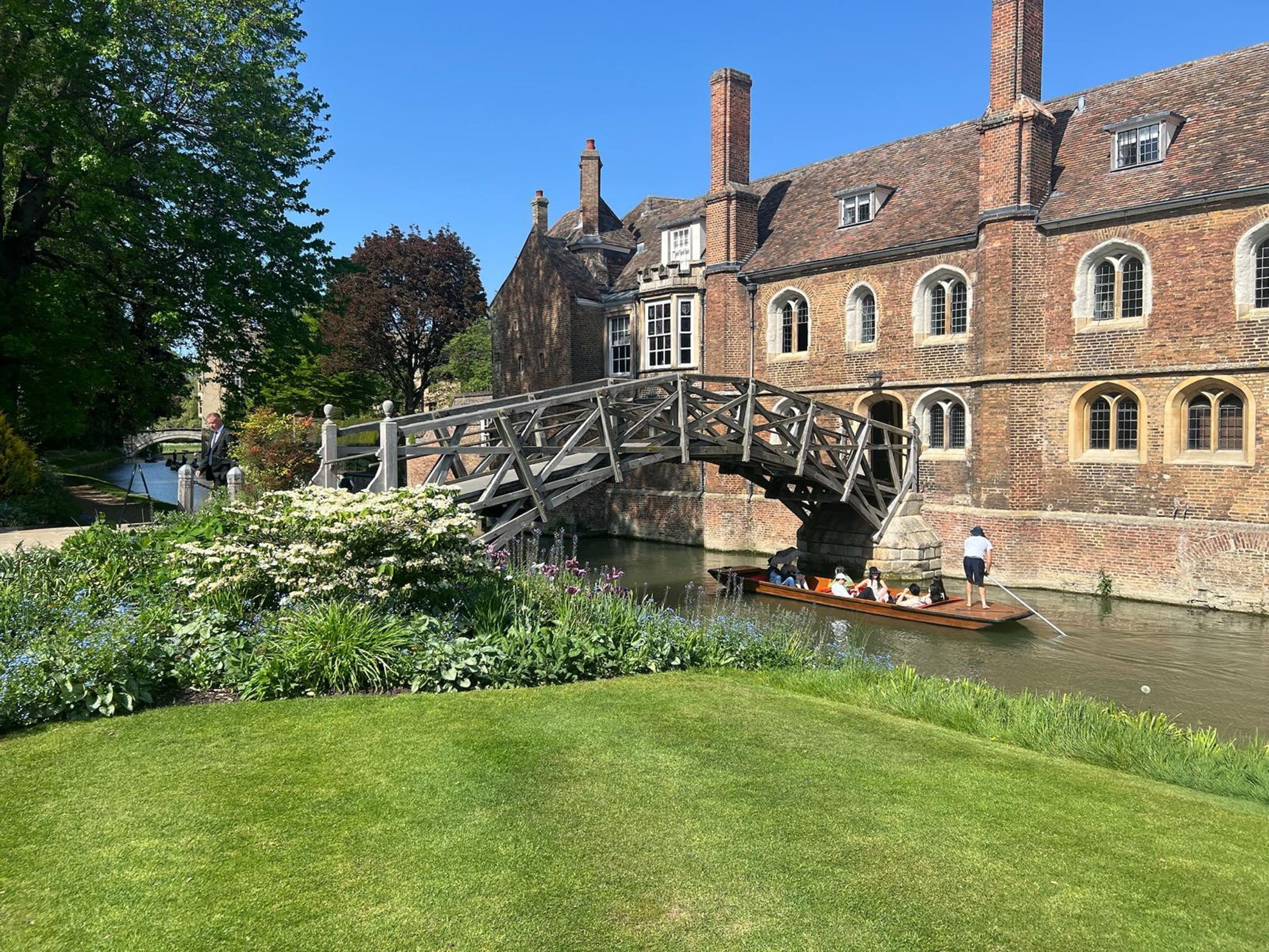 A historic building with a bridge over a canal, surrounded by well-maintained gardens and a grassy area.