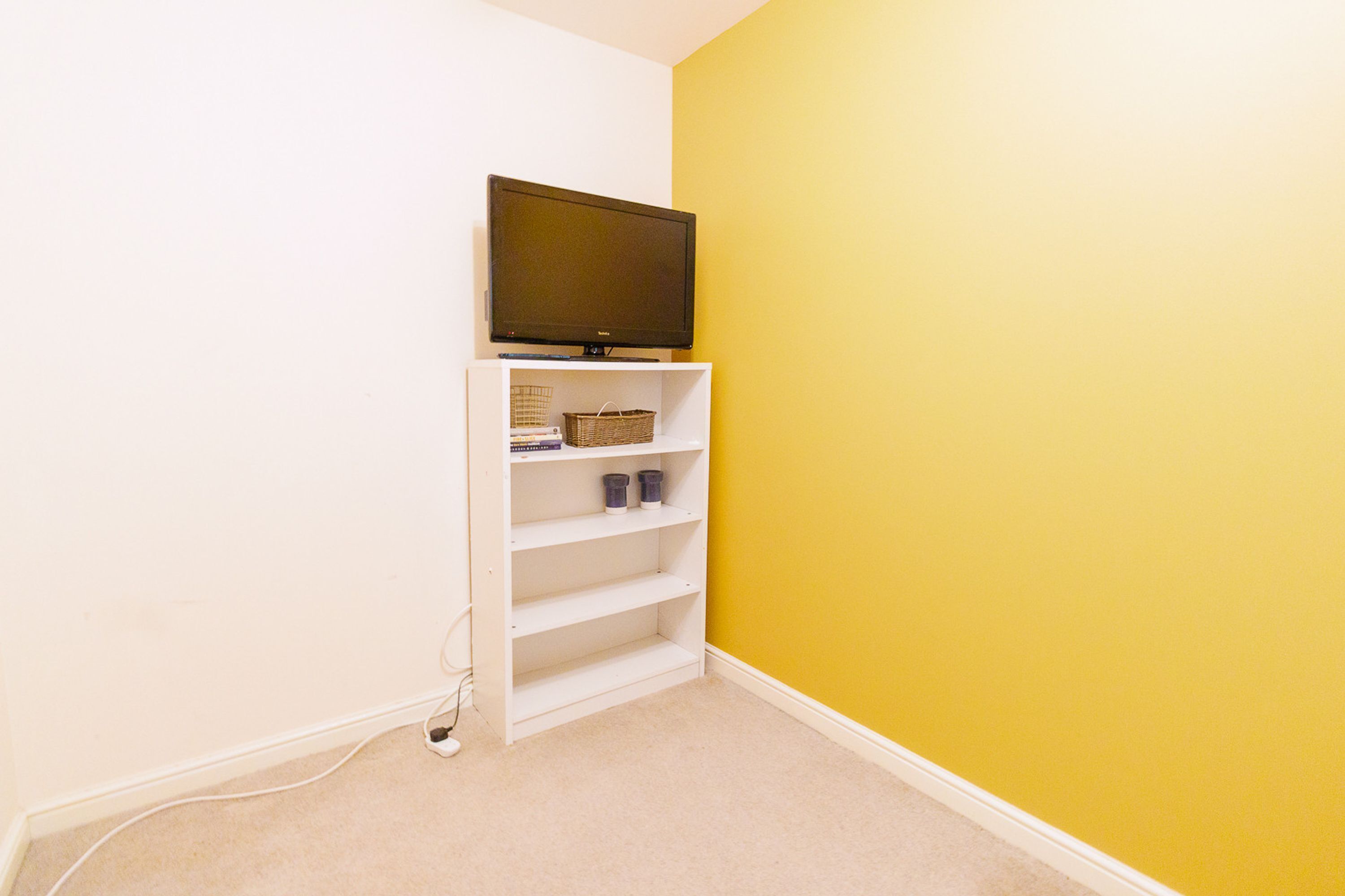 A room with a white entertainment unit against a yellow wall, featuring a television, shelves, and a basket.