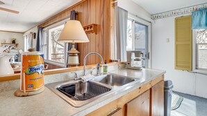A kitchen with wooden cabinets, a sink, a window with a curtain, and a towel dispenser.