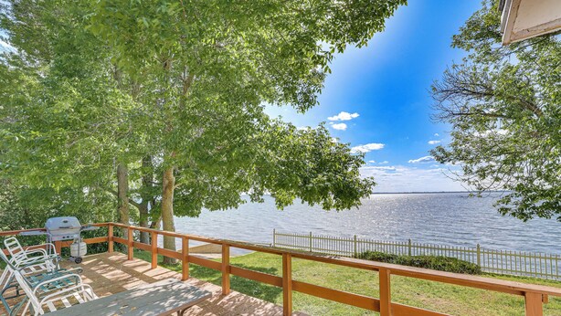 A wooden deck with a view of a lake, a grill, and outdoor seating.