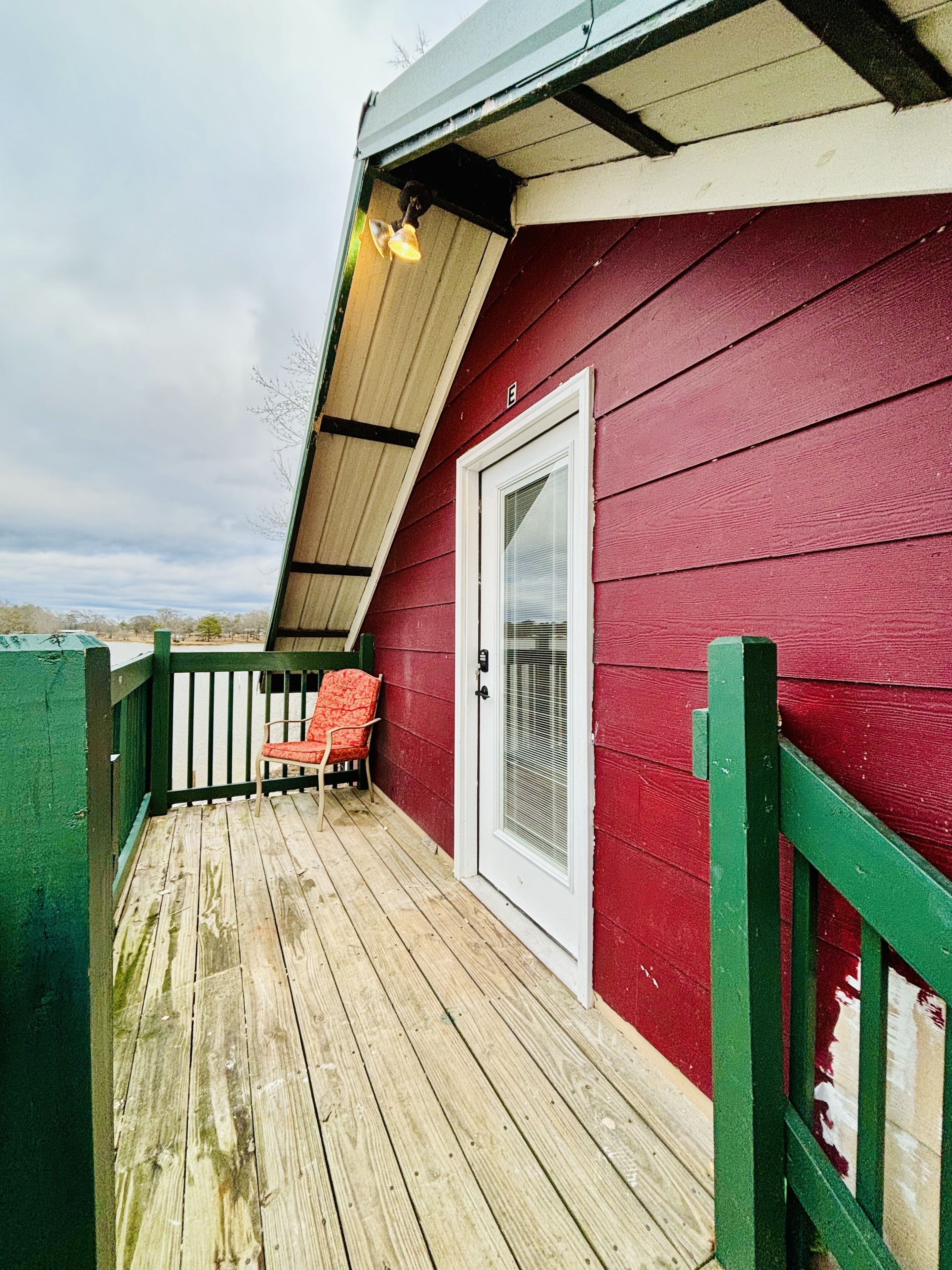 A red building with a white door, a wooden deck, and a green railing.