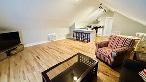 Un appartement-loft spacieux avec de hauts plafonds, un coin cuisine et un espace salon comprenant un fauteuil à rayures et une table basse.