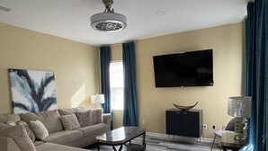 Ein modernes Wohnzimmer mit einer Eckcouch, einem Couchtisch, einem an der Wand montierten Fernseher und einer Stehlampe.
