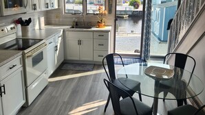 Una cocina moderna con armarios blancos, microondas integrado y un comedor con mesa de vidrio y sillas negras.
