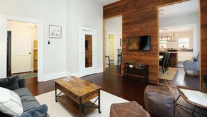 Una sala de estar con una mesa de centro de madera, un sofá, un televisor y una cocina al fondo.