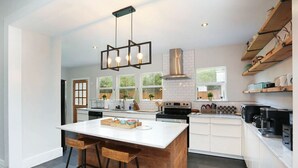 Una cocina moderna con una isla central, taburetes de bar, estufa integrada y una lámpara colgante.