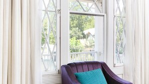 Ein Zimmer mit einem violetten Sessel und einem Fenster mit weißen Vorhängen.