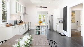 Eine moderne Küche mit weißen Schränken, einem Esstisch mit Stühlen, einem Deckenventilator und Blick ins Freie.