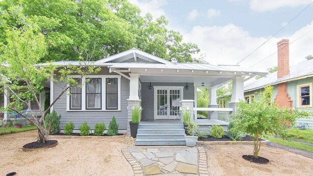 Une maison à deux étages avec un porche à l’avant, un chemin de pierre menant à l’entrée et un petit jardin avec différentes espèces de plantes.