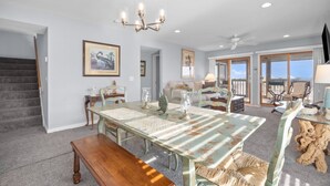 A spacious dining area with a large table, chairs, and a chandelier. There is a staircase leading to another level. - Oceanview, Pet Friendly in Pelican Point (Saint Helena Island)