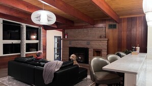 A cozy living room with a fireplace, a black leather sofa, and a dining area with chairs and a table.