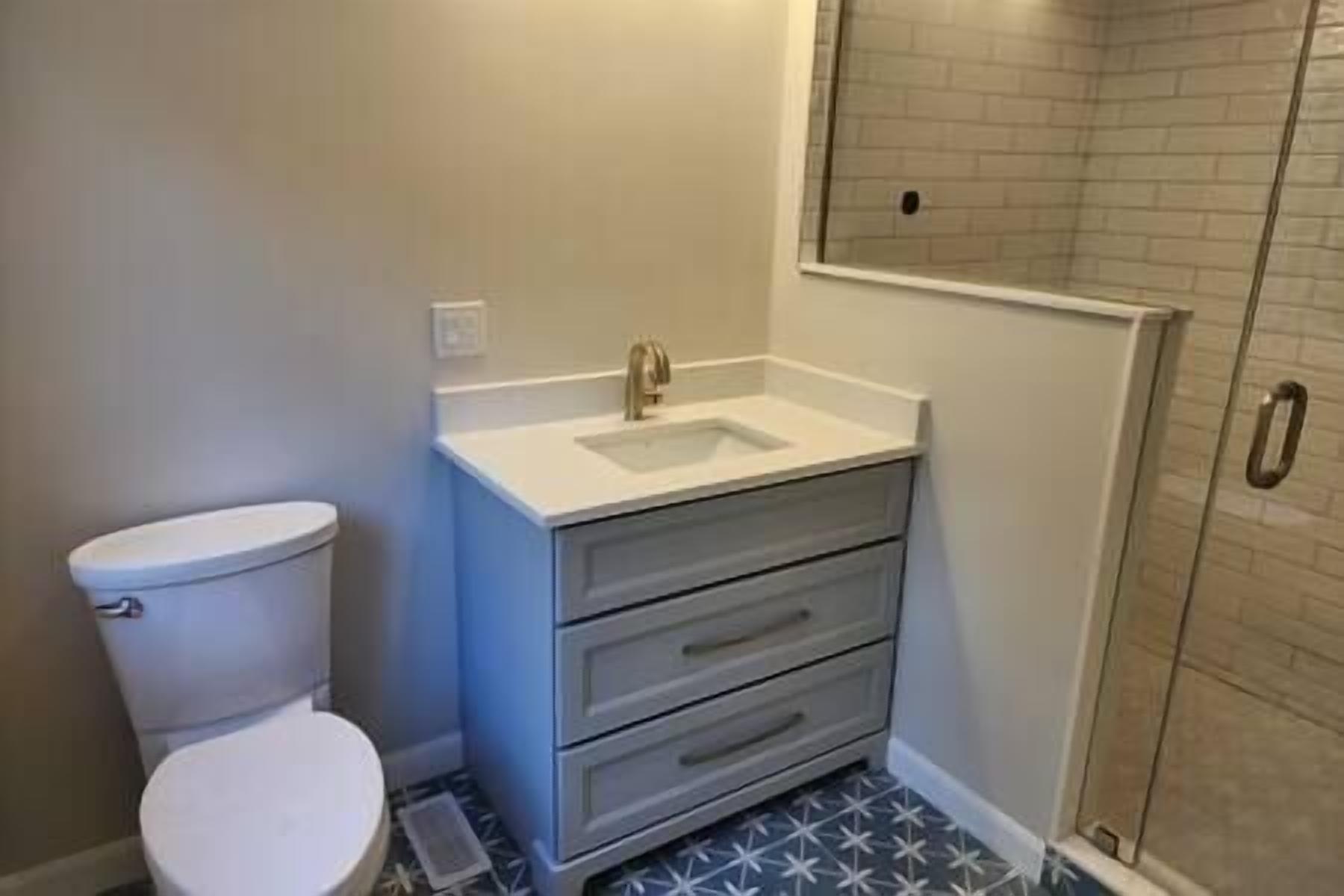 A bathroom with a toilet, a sink with a mirror, and a shower area.