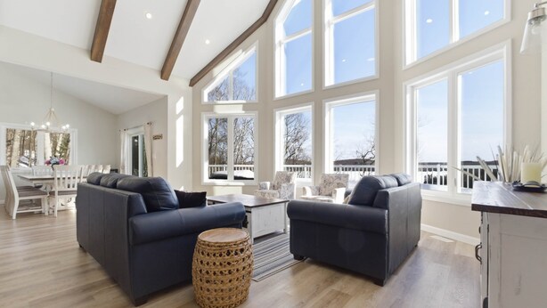 Ein geräumiges Wohnzimmer mit zwei dunklen Sofas, einem Holzessttisch und großen Fenstern mit Blick ins Freie.