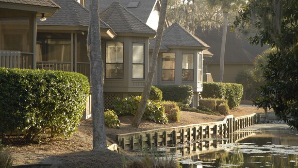 A residential area with a house featuring a covered porch, a small pond, and a wooden bridge. - Port O'Call - Hilton Head 6/21/25-6/28/25 - HUGE DISCOUNT!!

 (Hilton Head Island)
