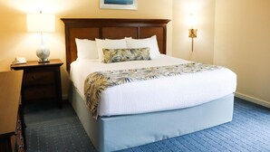 A hotel room with a large bed, a nightstand with a lamp, a wall-mounted light, and a framed picture above the bed. - Port O'Call - Hilton Head 6/21/25-6/28/25 - HUGE DISCOUNT!!

 (Hilton Head Island)
